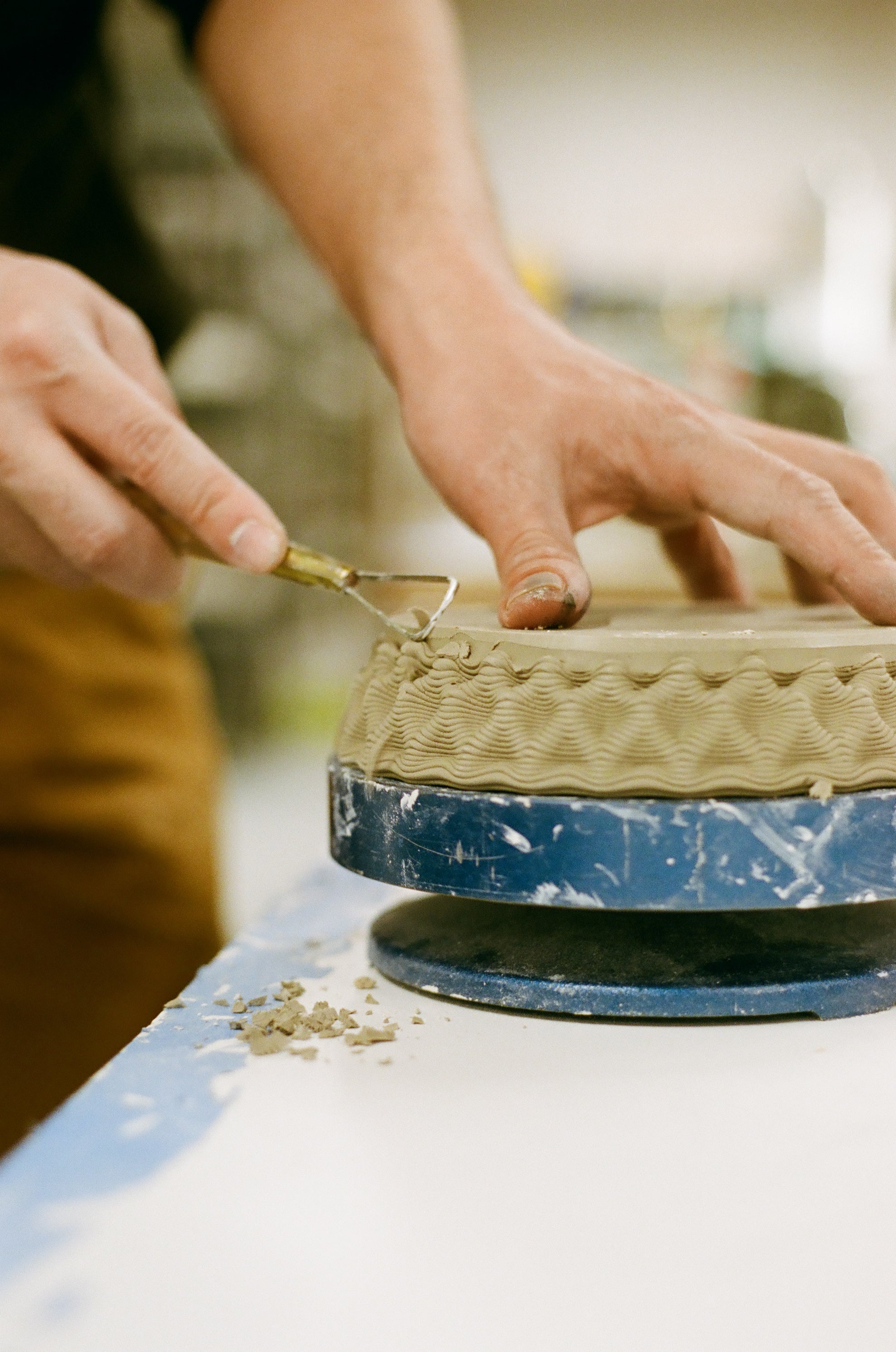 Person working on a ceramic piece using a tool on a pottery wheel.
