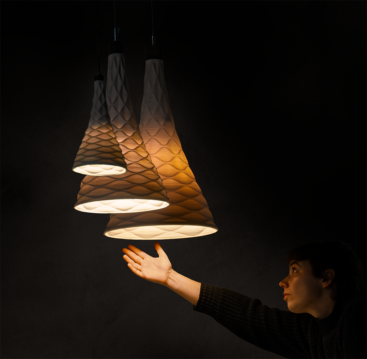 Three pendant lights with a diamond textured design hanging above a person's outstretched hand against a dark background.