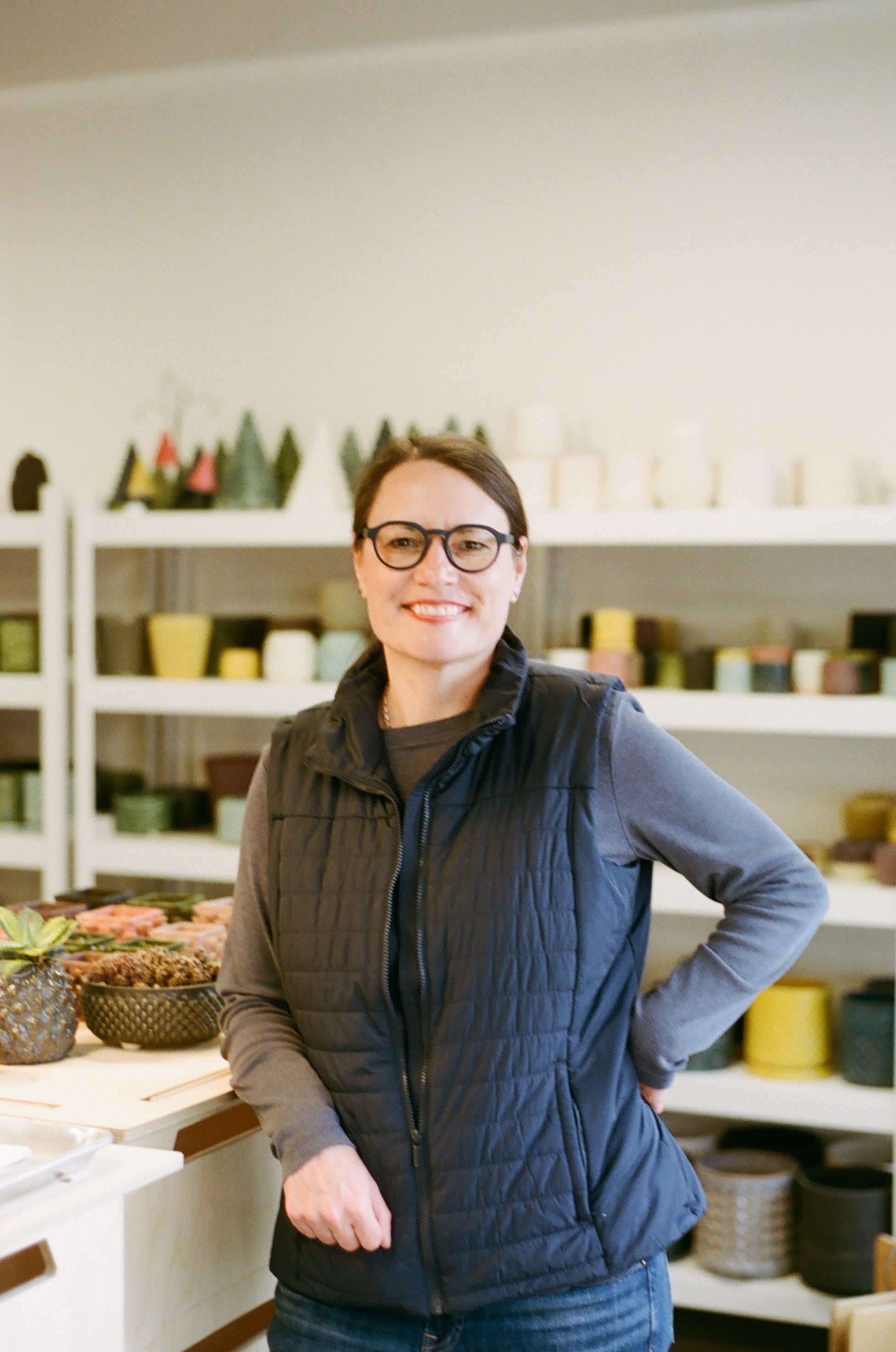 Person wearing a dark vest and glasses in a store setting with shelves in the background